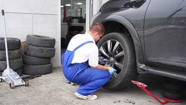 Auto mechanic installs tire on vehicle using air wrench at service station. Worker fastens lug nuts, aligns wheel, ensures car safety. Garage pro replaces rim, conducts maintenance.