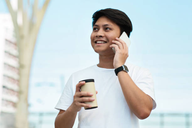 istock Happy young asian man talking on smartphone, drinking coffee 1915346302