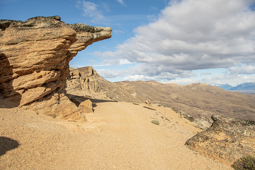 A barren desert trail meandering amongst rocky and gravel terrain, with majestic mountain peaks in the background