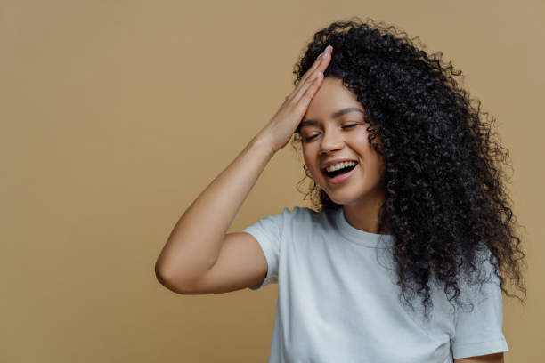 istock Laughing woman with hand on forehead, casual white tee, beige backdrop 1915360610