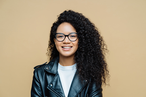 Smiling woman in glasses and leather jacket, beige background