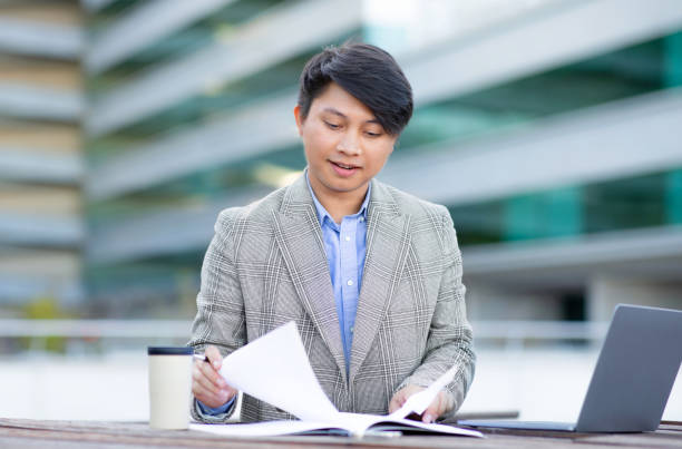 istock Asian entrepreneur man reviews documents working online on laptop outside 1915363823