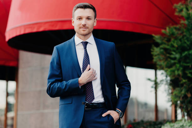 istock Professional man in blue suit, adjusting tie, urban backdrop 1915376748