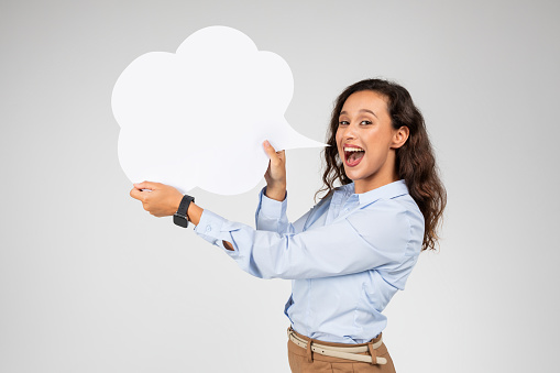 Cheerful adult european woman in formal with open mouth screaming, holding abstract cloud for words and thoughts, text, isolated on gray studio background. Ideas solution, sale, good news