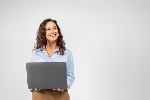 Positive caucasian millennial businesswoman typing on computer, chatting, look at empty space, isolated on gray studio background. Work, business, technology for startup, online courses