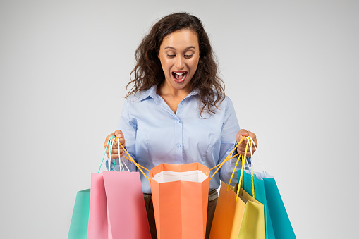 Shocked glad millennial european lady in formal wear with open mouth look at many shopping bags, enjoy shopping, isolated on gray background studio background. Surprise sale, buy clothes, fashion