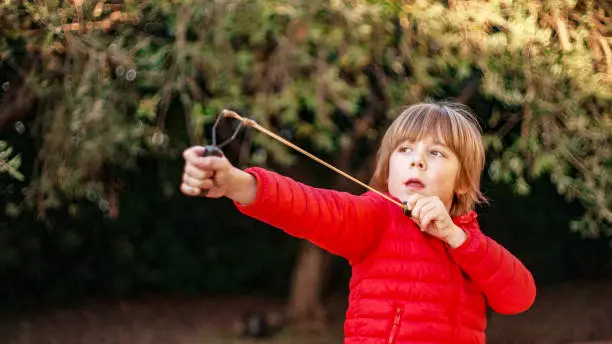 7 year old boy enjoys playing with the slingshot outdoors