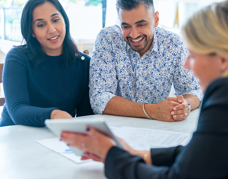 Mature couple meeting with financial advisor or real estate agent at home. They are sitting at the dining table at a paper work document a digital tablet presentation.