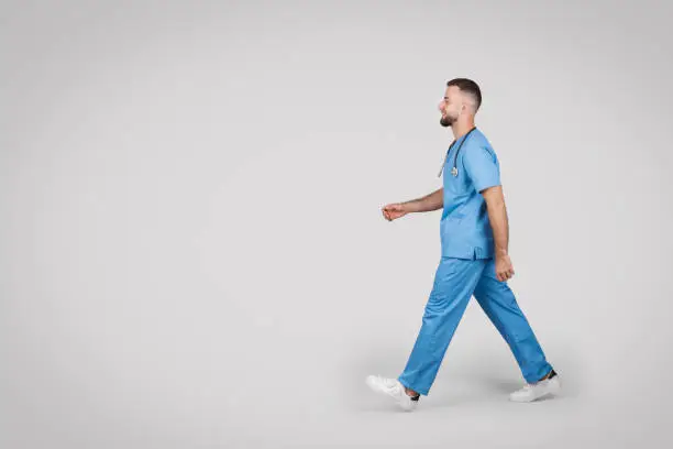 Dynamic side view of a male nurse in blue scrubs walking with purpose, depicting motion and active healthcare professional on the go, free space