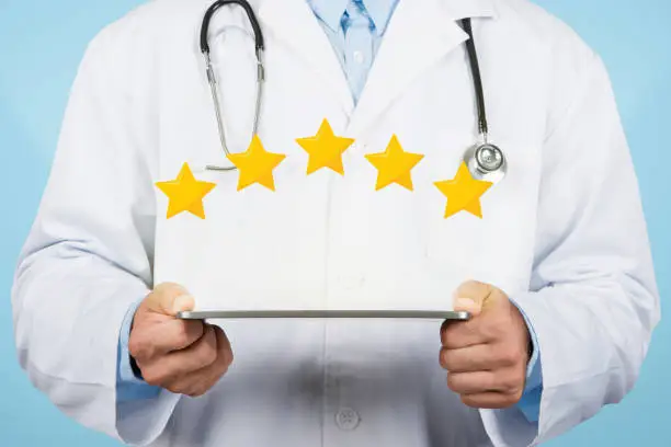 Photo of Doctor man holding tablet displaying five-star rating, blue background