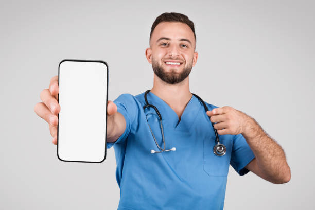 istock Cheerful doctor man showing blank phone screen and pointing at it 1915422165