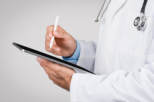 Close-up of medical professional using a stylus pen on a digital tablet, symbolizing modern digital healthcare documentation and telemedicine