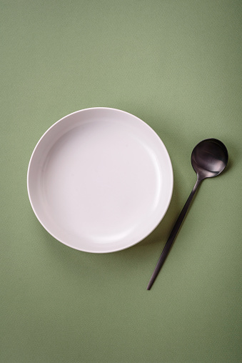 Empty round ceramic plate on a plain background, flatley with copy space. Kitchen utensils in home kitchen