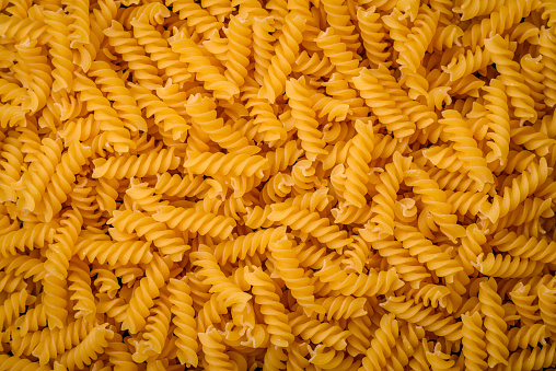 Raw fusilli pasta from whole grain wheat varieties on a dark textured background