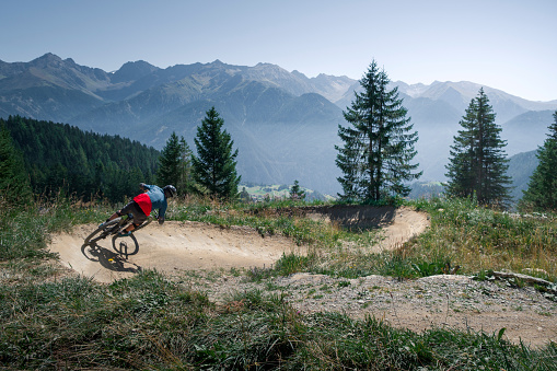Downhill mountain biking on a shaped bike park trail in Austria, sunny blue sky day, trees and mountains in background