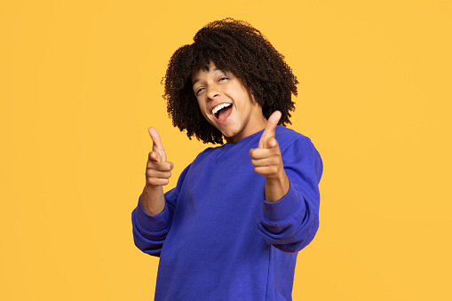 Portrait Of Cheerful Excited Black Guy Pointing At Camera With Two Hands, Emotional Black Man Indicating Somebody, Shouting Gotcha While Standing Isolated Over Yellow Studio Background, Copy Space