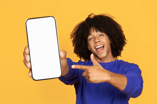 istock Online Ad. Cheerful Black Guy Pointing At Blank Smartphone In His Hand 1915482013