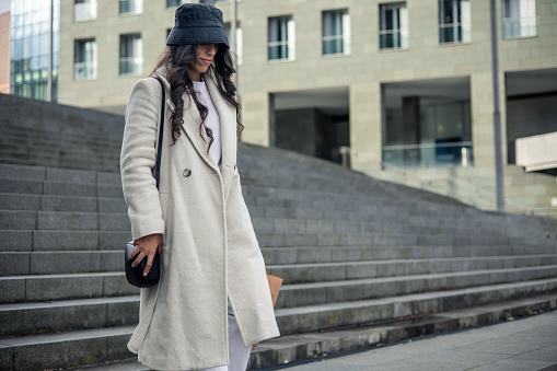 successful caucasian woman walking down steps with hat and coat after work