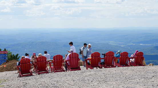 Sightseeing mountain views at Mont Tremblant ski Resort in summer. Tourists enjoying sitting at red chairs at ski resort village. Mont-Tremblant, Quebec, Canada - 22.09.2022.