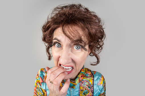 A funny fisheye image of a middle aged woman in a vintage paisley robe and 1960s hair fashion nervous and biting her nails.