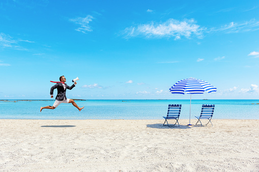 Happy businessman running on the tropical beach with megaphone. Summer vacation concept.