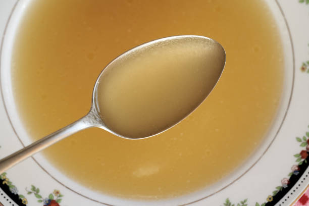 Chicken bone broth on a spoon above a soup bowl, top view