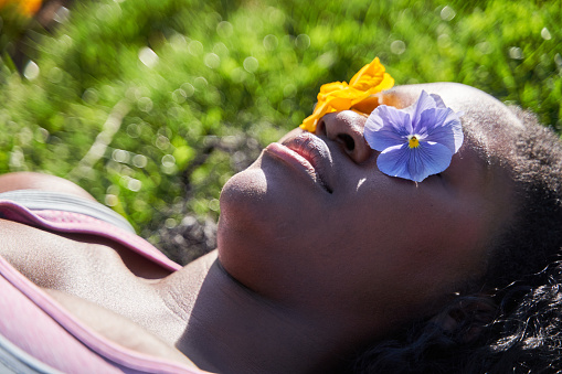 african-american woman lying on the grass with two flowers covering her eyes