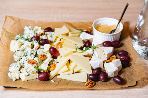 An elegant cheese board featuring a variety of cheeses, walnuts, grapes, and a side of honey, perfect for entertaining.
