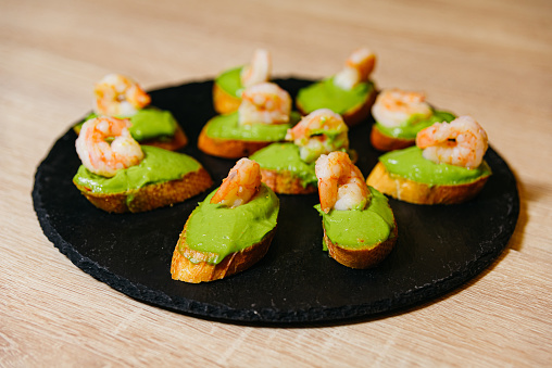 A black plate topped with mini shrimp and guacamole. Catering presentation. A Mouthwatering Delight.