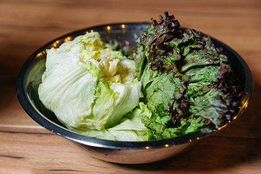 A stainless steel bowl overflowing with crisp green and purple lettuce leaves, ready for a nutritious salad preparation.