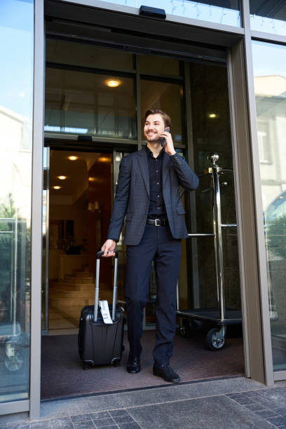 istock Cheerful man talking on phone while leaving hotel 1915660705