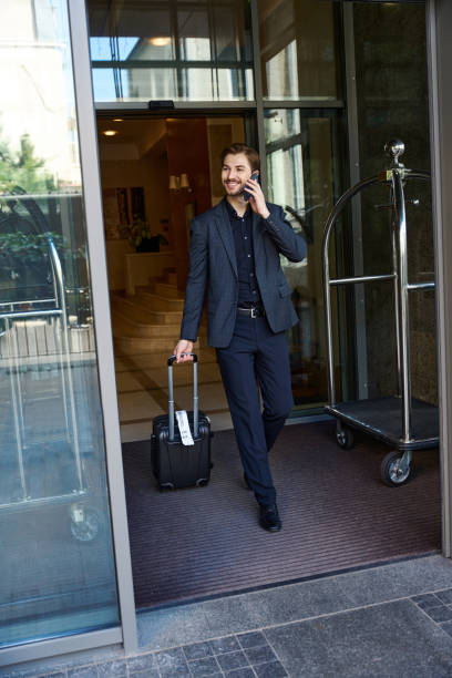 istock Smiling man talking on phone when going outside hotel 1915660709