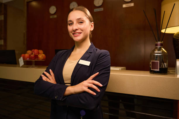 Cheerful woman receptionist folded hands across chest while standing near reception desk in hotel