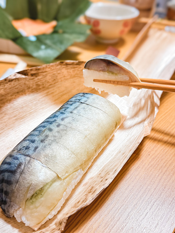 A whole row of mackerel sushi, with a pair of chopsticks picking up one piece.