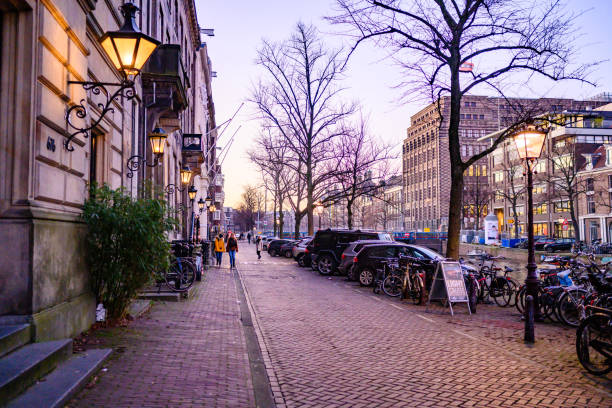 In Amsterdam, Netherlands at dusk lanterns on the building exterior illuminate the dark sidewalk with bare trees in winter.