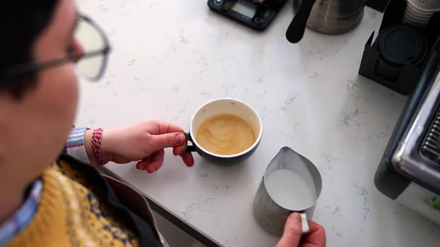 High angle view of a female barista pouring milk cream into espresso coffee