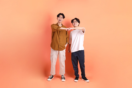 The Adult east 20s two friends with braces standing on the pink or orange background.
