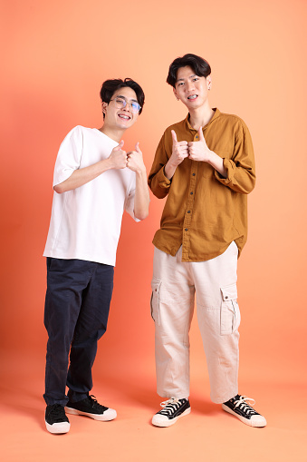 The Adult east 20s two friends with braces standing on the pink or orange background.