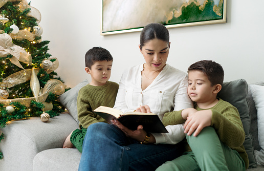 Young Latin mother reading to her small boys on Christmas day.