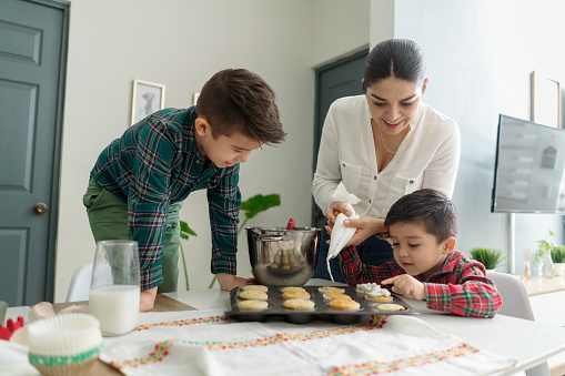 Young Latin mother decorating cupcakes with her children.