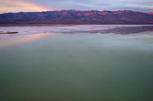 Witness the magical sunrise at Bad water Basin in Death Valley National Park, California. As the first light kisses the vast salt flats, gaze upon the stunning panorama with Telescope Mountains in the distance, creating a serene and unforgettable moment