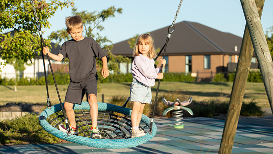 Brother and sister are playing on the playground outside. Children ride on a swing. The concept of a happy childhood.