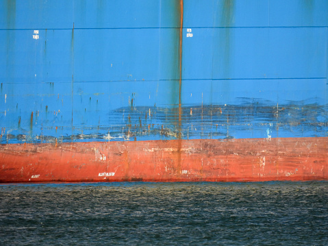 The hull of the Cosco Singapore container ship showing the marks of docking and general wear-and-tear.  She is docked at Port Botany Container Terminal in Sydney.  This image was taken from Mill Stream Lookout, Botany Bay, on a sunny afternoon on 6 January 2024.