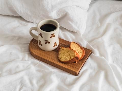 Lazy morning in bed - a mug of black coffee and pieces of orange cupcake on a wooden tray on the bed
