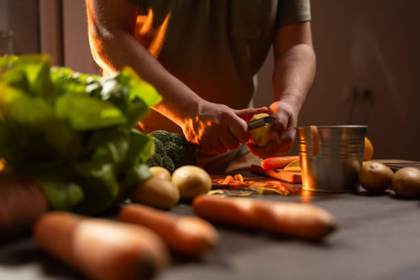 Close-up shot of unrecognizable man peeling potato on the table while preparing lunch at home