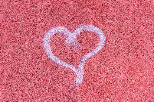 Closeup of white heart hand-drawing on a pink textured stucco wall. Symbol of love and romance. Background with copy space