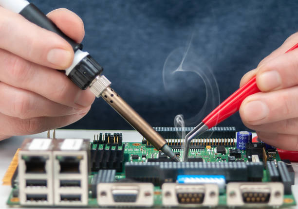 Close up of a technician's hands in a workshop. Repairer is soldering circuit board of electronic device on table with tweezers.