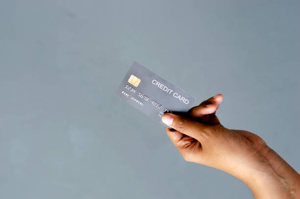 istock female hand holding a black credit card mockup with security chip embedded on a gray background with copy space 1916478694