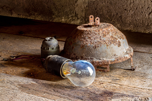 Old rusty lighting fixtures. A burnt-out light bulb. Electric lighting fixtures on a rough wooden surface.