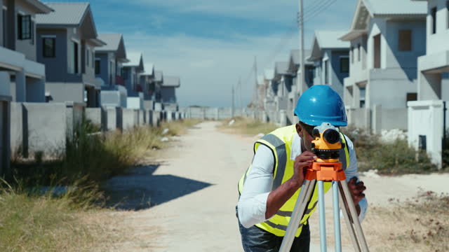 African civil engineer is using a survey telescope to measure the level on construction site to plan the house construction project.
